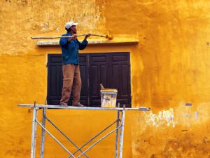 Pintor aplicando rodillo en pared interior con ventana abierta durante el verano